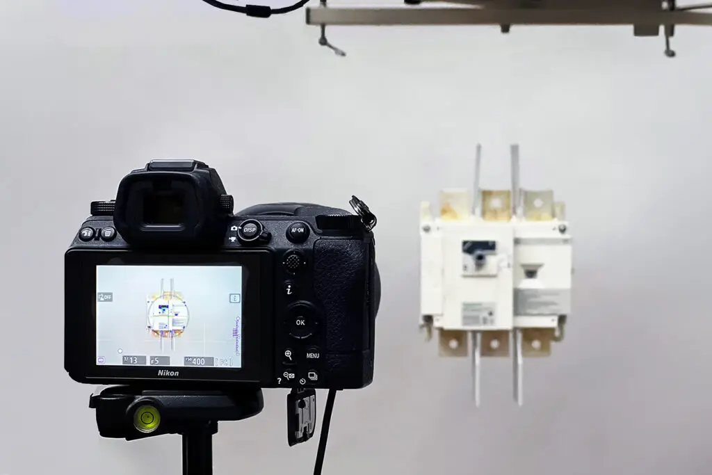 Behind the scenes commercial product photography workflow showing tethered camera capturing suspended industrial component in studio